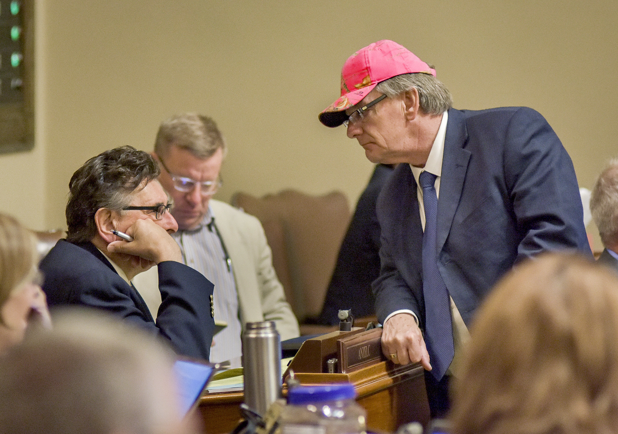 Donning a blaze pink hat, Rep Tom Hackbarth confers with Rep. Tom Anzelc during a recess May 18.  Minutes prior, the House passed a bill Hackbarth sponsors that would make it legal for hunters to wear blaze pink, in addition to blaze orange. Photo by Andrew VonBank